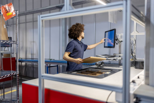 istock Young man holding a box and updating package details on computer at automated warehouse 1581300082