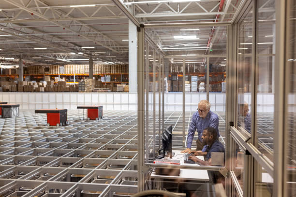 Man operating AGV in control room in warehouse with manager standing by