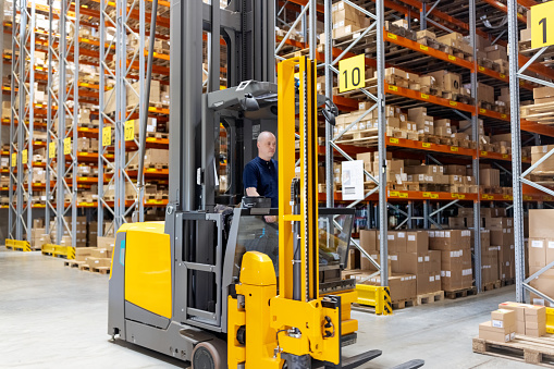 Male worker working on forklift loading machine in distribution warehouse. Forklift operator in a large distribution warehouse.