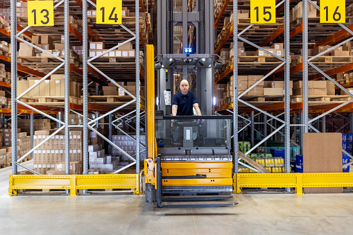 Man operating a forklift loader in a distribution warehouse. Worker working in factory storage room driving a forklift machine.