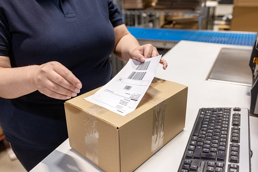 Close-up of female worker sticking a label on a delivery box. Warehouse worker working in distribution warehouse preparing a package for delivery.