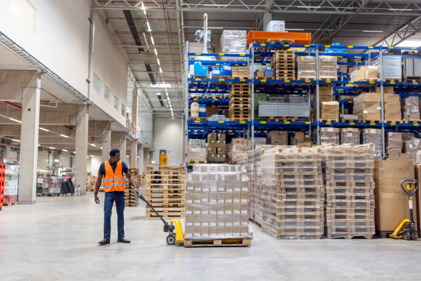 istock Worker moving cardboard boxes on pallet jack in a warehouse. 1581300448