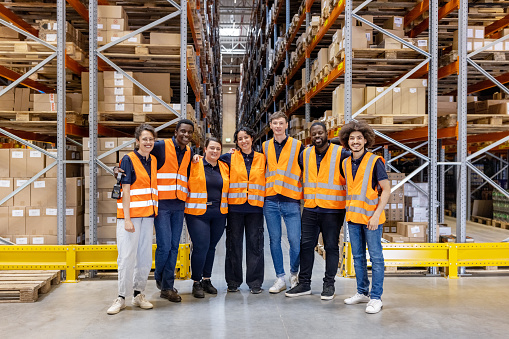 Portrait of multi-ethnic warehouse workers standing together. Team of workers in reflective clothing working at distribution warehouse.