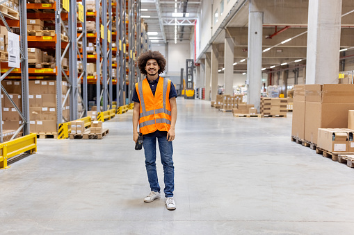 Portrait of a confident young man working in distribution warehouse. Happy warehouse worker standing in large storage facility.