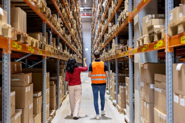 istock Businesswoman with worker walking through a distribution warehouse checking stock 1581310060