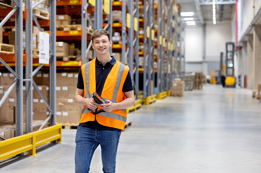 Portrait of a confident young worker with bar code reader in a distribution warehouse.  Happy male worker standing in the supply chain storage center.