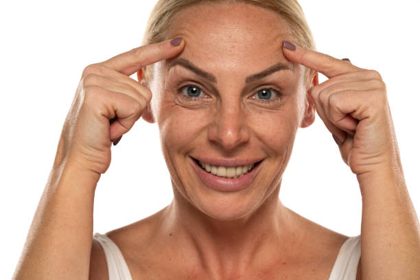 portrait of a beautiful middle aged senior  woman, lift her eyebrows with her fingers on a white background stock photo