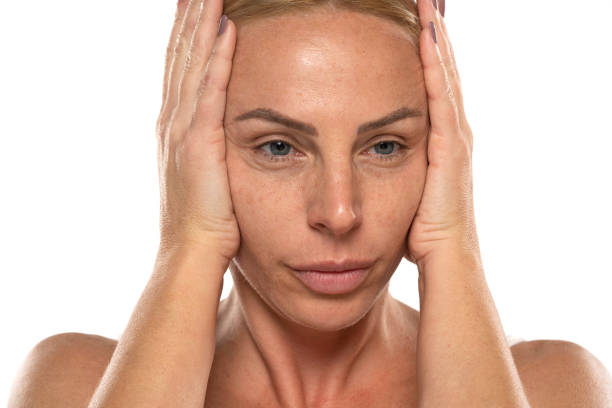istock Middle aged blond woman tightens her face with her hands on a white background 1581372853