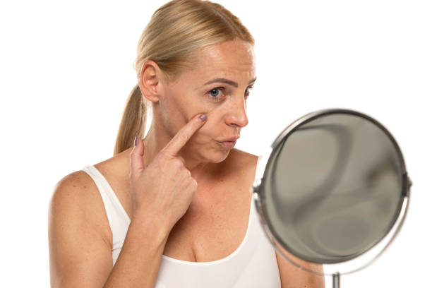 istock Middle aged woman checking her eye in the mirror on a white background 1581372855