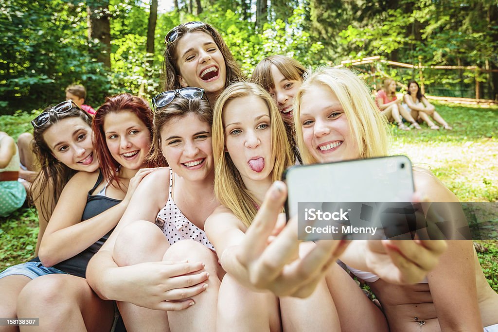 Girls Together Summer Camp Snapshot Happy Summer Camp. Group of girls sitting together in the grass, making a funny snapshot with a mobile phone camera. Summer Camp Stock Photo