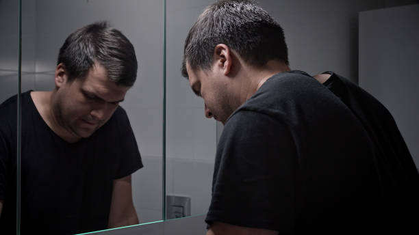 istock Upset lonely man suffering from depression looking in reflection at bathroom mirror. Concept of depression, suicide, stress, mental illness, loneliness and frustration. 1581394671