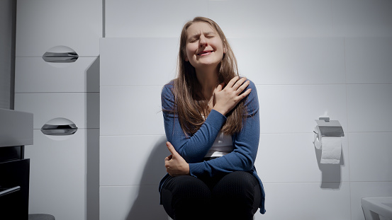 Portrait of woman suffering from depression crying on toilet at home. Concept of depression, home violence, suicide, stress, loneliness and frustration