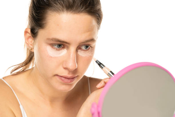istock Young woman applyes concealer under her eyes on white background 1581428239