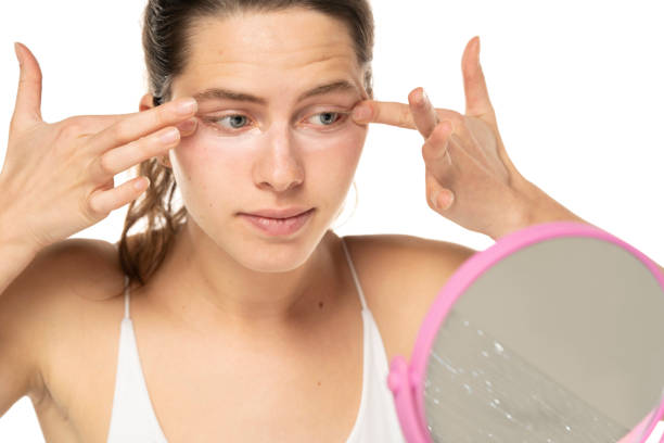 istock Young woman applyes concealer under her eyes on white background. 1581428244