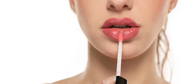 Close up of beautiful young woman applying lipgloss on a white background.