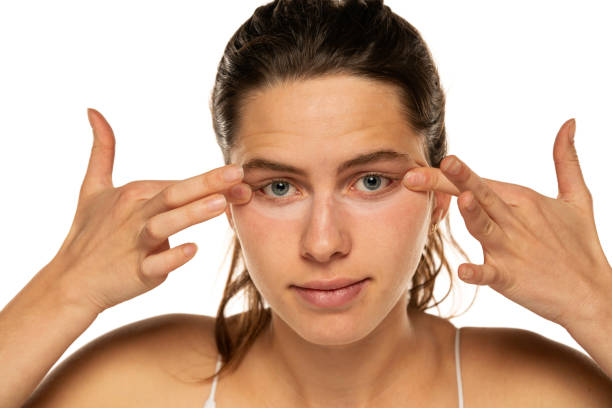 istock Young woman applyes concealer under her eyes on white background 1581428721