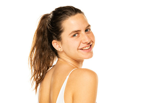 Portrait of a young smiling woman with ponytail and without makeup on a white background.