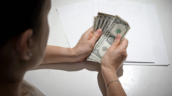 CLoseup of young woman having financial diffuculties counting her money behind kitchen table.