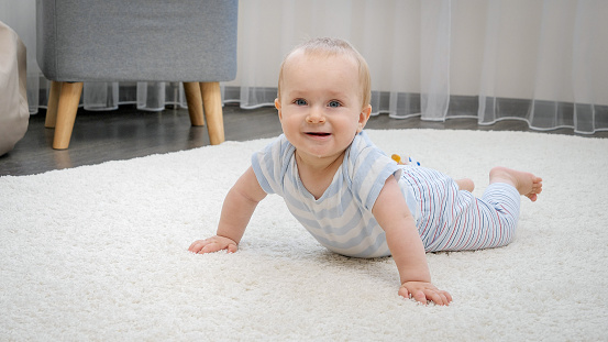Happy smiling baby boy lying on soft carpet in living room. Concept of child development, happy childhood and fun at home