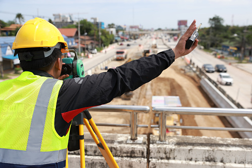 Civil or survey technician working at a new road construction site with a walkie-talkie and survey camera.