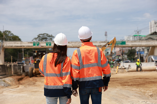 Back view of two civil engineers walking and discussion on the construction site of the new road construction.