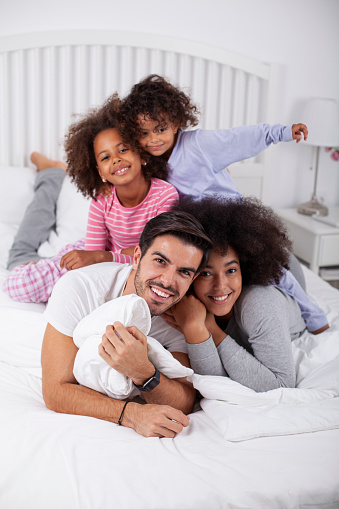 Happy mixed race family lying on bed and looking at camera