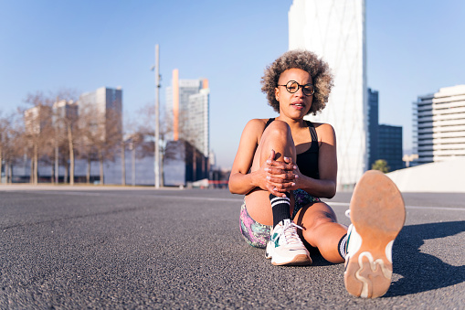 african american woman stretching the legs sitting in an urban park, concept of health and sportive lifestyle, copy space for text