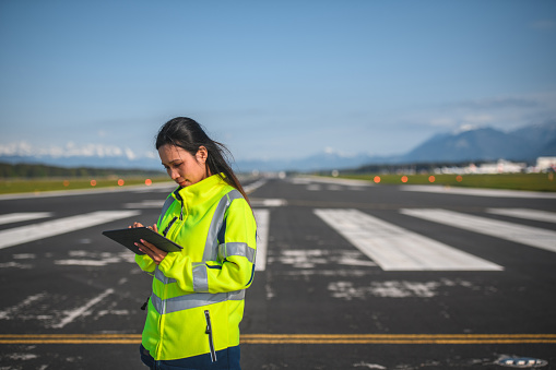 Portrait of an Asian female airfield operations officer standing on a runway with using a digital tablet.