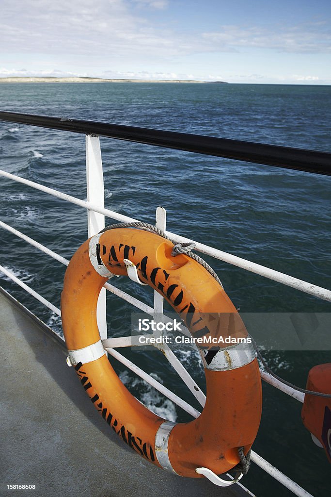 Life Preserver in Patagonia Image of the railing of a boat in front of bright green waters. Orange life preserver ring features the words "Patagonia Valparaiso." Valparaiso is a city off the coast of Chile.  Barge Stock Photo