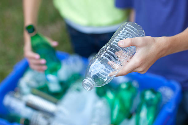 Hands placing bottles in recycling bin Caucasian boy and girl putting clear and green bottles and metal cans in recycling blue bin outside in yard plastic stock pictures, royalty-free photos & images