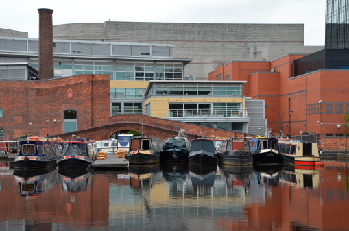 Boats standing on calm water in the Birmingham Canal Navigations. In background  visible characteristic brick buildings.
