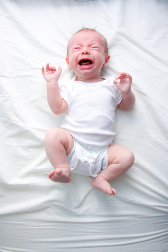 Crying newborn on white bed sheet wearing white onesie