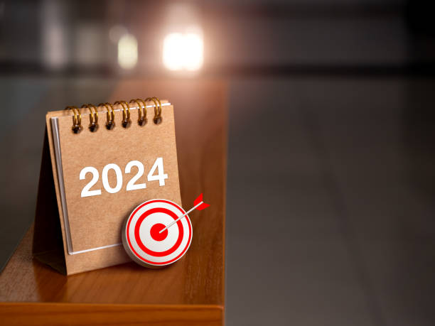 Happy new year 2024 banner background. 3d target icon with 2024 numbers year on brown small desk calendar cover standing on table edge with sunlight and copy space. Business goal and success concepts. feliz año nuevo 2024 banner de fondo. icono de destino 3d con números 2024 año en marrón pequeña cubierta de calendario de escritorio de pie en el borde de la mesa con luz solar y espacio de copia. objetivo de negocio y conceptos de éxito.