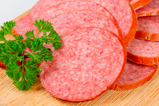 heap of fresh sliced salami with a parsley on a wooden cutting board