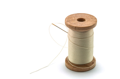Isolated wooden spool of cream thread with a needle