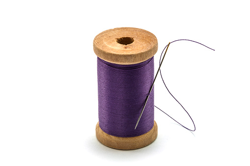 Isolated wooden spool of light purple thread with a needle