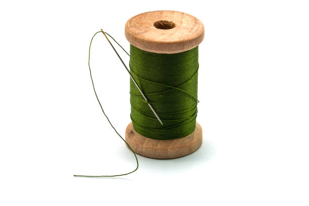 istock Isolated wooden spool of green thread with a needle 1581921046