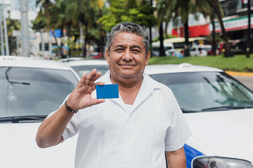 latin taxi driver man holding blank card with car on background at city street in Mexico in Latin America, Hispanic adult senior people