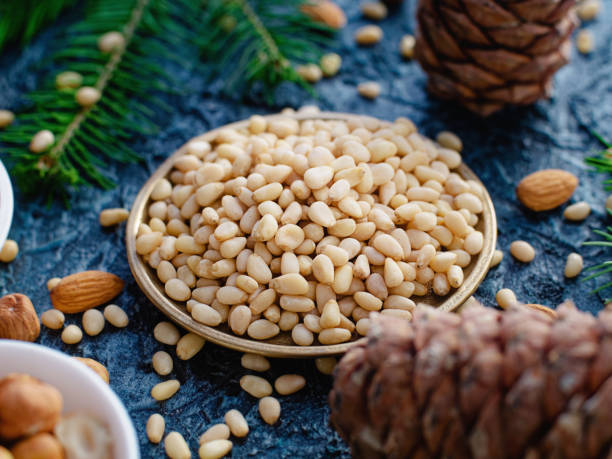 istock Peeled pine nuts lie in plate among cones. Still life of pine nut kernel. 1581954730