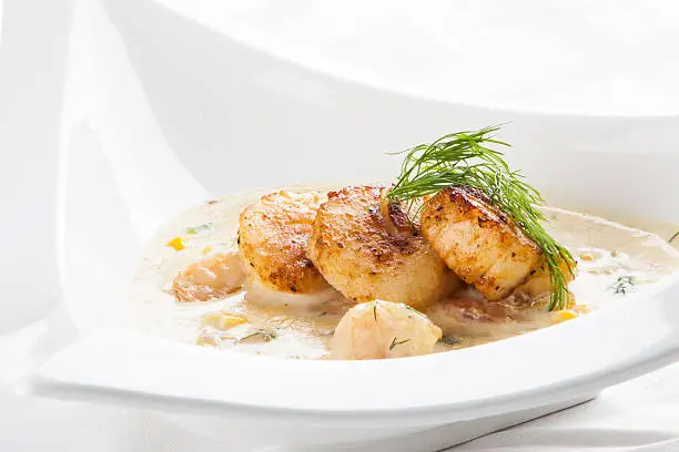 A creamy shrimp and clam bisque topped with seared sea scallops and garnished with dill.