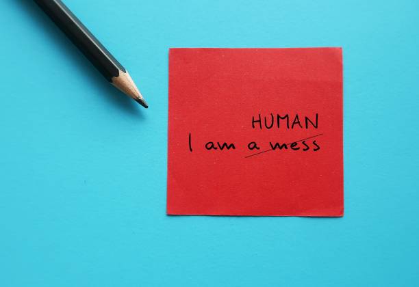 istock Red note on blue background with handwriting I AM A MESS, croffed off to I AM HUMAN - to overcome negative self talk or inner voice critic, change to positive thought to boost self esteem 1582008489