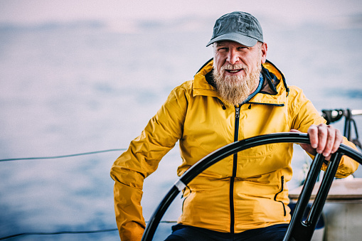 Confident skipper sailing on sailboat holding steering wheel.