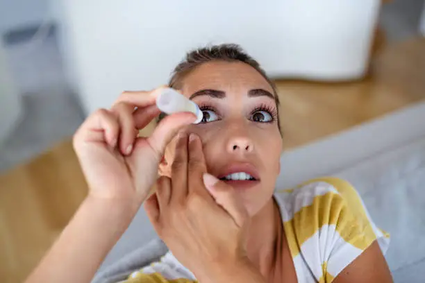 Woman using eye drop, woman dropping eye lubricant to treat dry eye or allergy, sick woman treating eyeball irritation or inflammation woman suffering from irritated eye, optical symptoms