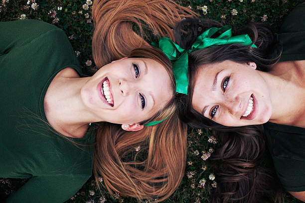 Sisters Laughing and Laying Down Two girls laying down on the grass laughing upwards towards the sky. It might be st. patricks day because of the green bows in their hair. st. patricks day photos stock pictures, royalty-free photos & images