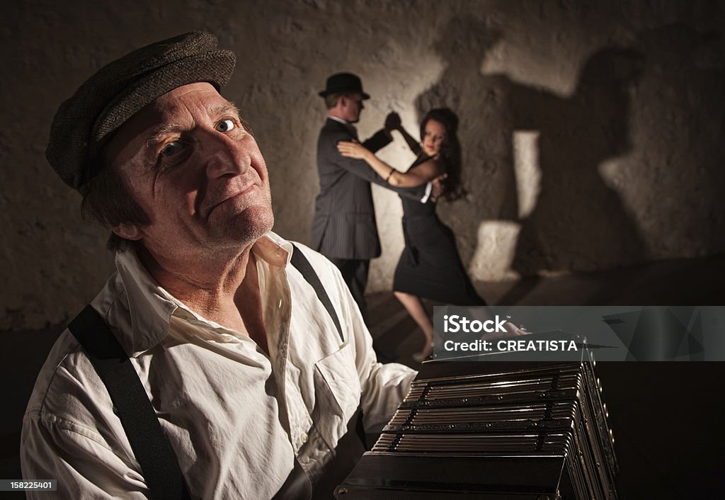 Smiling Accordion Player with Dancers Smiling accordion player performing with dancers in the background Argentina Stock Photo