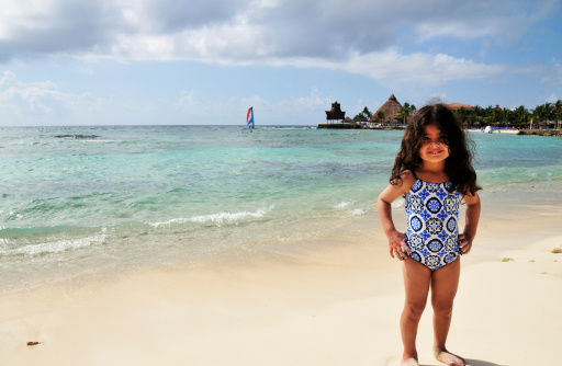 A little girl in a colorful one piece bathing suit on the white sandy beach in Riviera Maya, Mexico