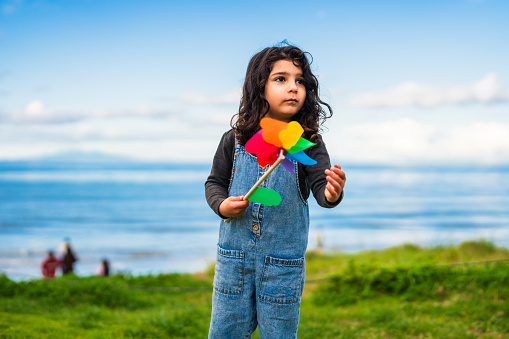 Portrait of cute little girl in public park playing with a pinwheel toy.