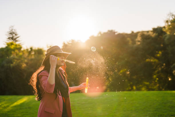 Woman  in the public in casual wear blowing soap bubbles, enjoying a day out.