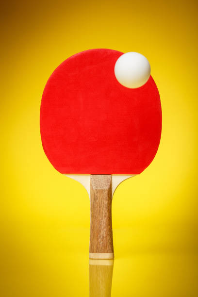 lado vermelho de uma raquete de pingue-pongue com uma bola branca em pé sobre um fundo amarelo. - racquette - fotografias e filmes do acervo