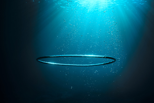 Underwater shot of big air bubble ring in deep transparent sea with shiny light during summer day